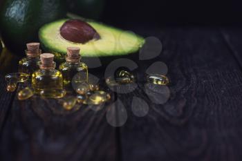 Oil of avocado with fish oil pills on a dark wooden background