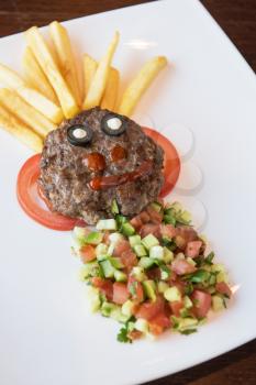 Funny meat cutlet face with french fries as hair and cutted vegetables for children menu