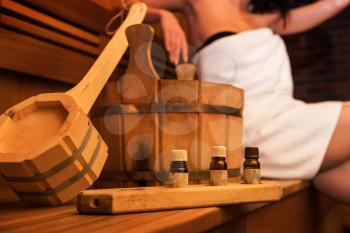 Wooden bath accessories with aromatic oil bottle for bath in the sauna and woman on background