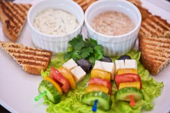 Tasty snacks: roasted toast with cheese vegetables and olive on the stick. Served with two kind of sauce