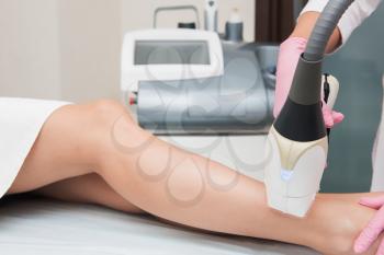 Closeup photo of woman getting laser hair removal procedure on her legs in modern clinic. Cosmetology and SPA concept