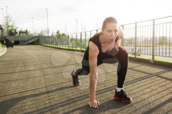 A woman in sportswear doing fitness exercises. City in sunny evening.