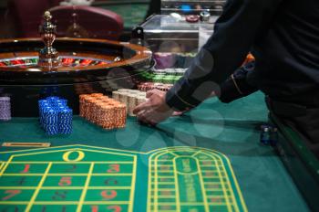 Casino, gambling and entertainment concept - roulette table and stack of poker chips