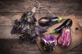 Aubergines and basil on chopping board in rustic style. autumn food photo