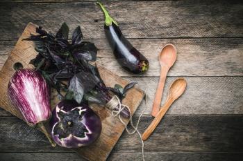 Aubergines with basil and spoons on wooden table. Rustic style and autumn food photo