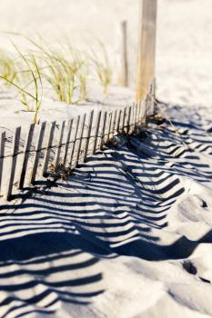 Wooden fence, grass and white sand dunes on the beach on a hot summer afternoon.