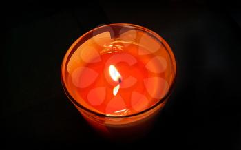 Bright orange burning candle in the dark