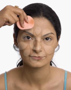 Person's hand applying powder puff on a young woman's face