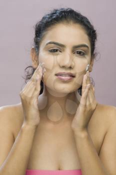 Portrait of a young woman applying moisturizer on her face