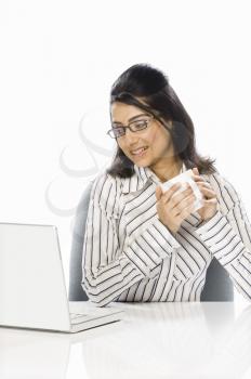 Businesswoman holding a coffee cup and looking at a laptop