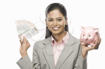 Portrait of a businesswoman showing Indian paper currency and a piggy bank