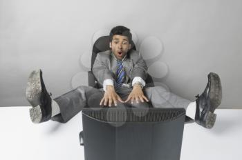 Businessman looking surprised with his feet up in front of a desktop PC
