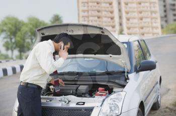 Businessman on the phone looking under the car hood