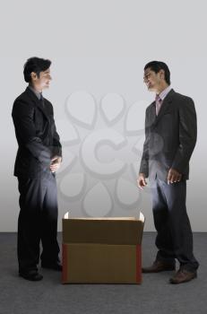 Two businessmen standing beside an illuminated cardboard box