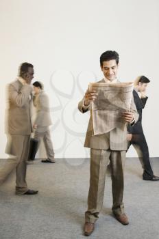 Businessman reading a newspaper with his colleagues in the background