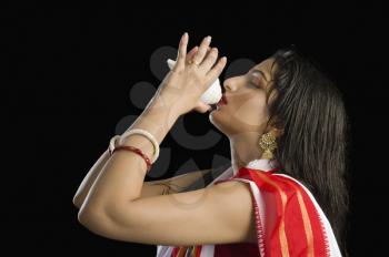Woman in a Bengali sari blowing conch shell
