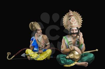 Two stage artists dressed-up as Rama and Ravana and talking on a mobile phone