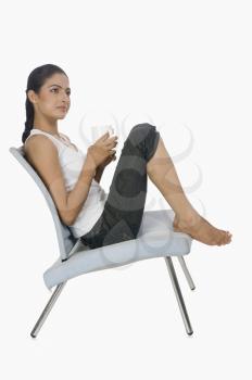 Woman holding a cup of tea and thinking on a chair