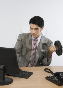 Businessman exercising with dumbbells and working on a computer