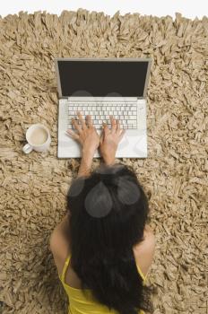 High angle view of a woman lying on a rug and working on a laptop