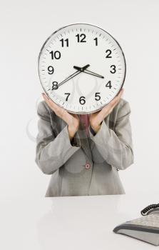 Businesswoman hiding her face with a clock