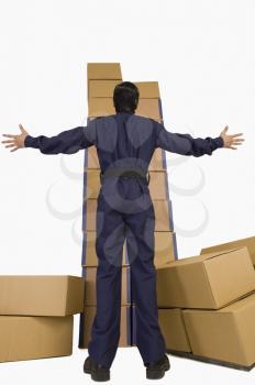 Rear view of a store incharge looking at a stack of cardboard boxes with his arm outstretched