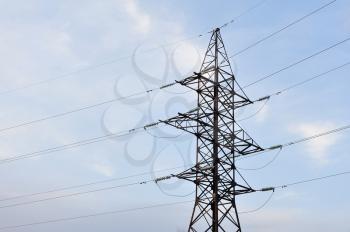 Large pole with power line wires against the sky with clouds