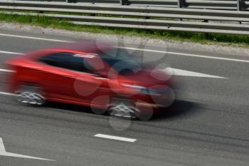 A red car at high speed rides along the road, blurred in motion