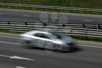 A silver car at high speed rides along the road, blurred in motion