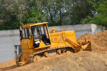 A bulldozer rakes the sand uphill in the warehouse.