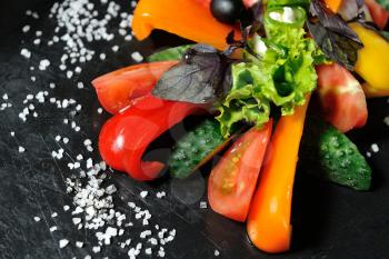 Sliced vegetables on a wooden board in a restaurant, cucumbers, tomatoes, peppers, lettuce leaves.