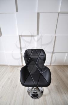 Beautiful bar chair, black, with elements of a triangle. The bar stool is black against a white wall with convex squares. Art space.