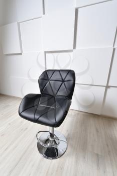 Beautiful bar chair, black, with elements of a triangle. The bar stool is black against a white wall with convex squares. Art space.
