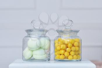 beautiful fresh yellow sugar dragees and marshmallows are stored in a glass transparent jars against the background of the white wall