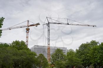 Construction cranes are building near the city park in the European city