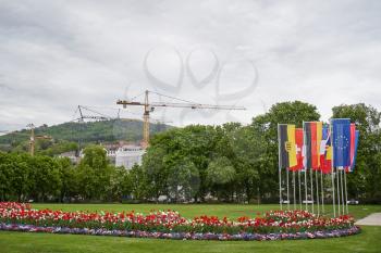 Construction cranes are building near the city park with flags of European countries and the European Union