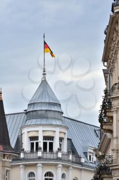 Flag of Germany on the high roof of the building against the background of a rainy sky.