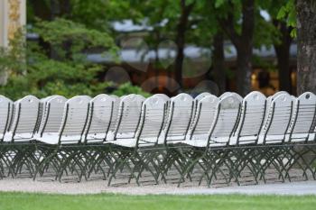 A group of white chairs, standing outside in the park in front of the stage.