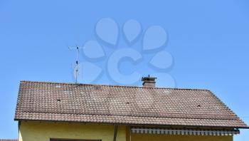 Roof with old tiles and a television antenna against the blue sky