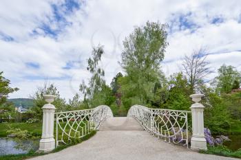 A hite forged iron bridge over a river in a public park in the European city of Baden Baden. Landscape with a bridge overlooking a green park