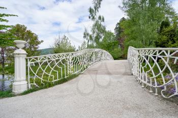A hite forged iron bridge over a river in a public park in the European city of Baden Baden. Landscape with a bridge overlooking a green park