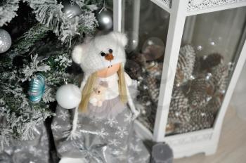 Children's cute stuffed doll stands next to the Christmas tree.