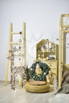 Children's playroom with wooden furniture, a house decorated for the New Year holiday with a Christmas tree, and a luminous deer from garlands.