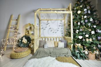Beautiful children's playroom with wooden furniture, a house and a staircase, decorated for the New Year holiday with a Christmas tree and a deer from a garland