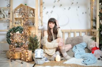 A young girl in woolen socks sits amid Christmas decorations in a children's play area