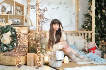 A young girl in woolen socks sits amid Christmas decorations in a children's play area