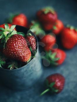 Ripe strawberries scattered around an iron mug