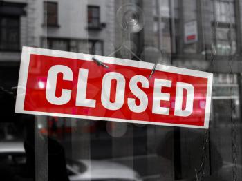 Closed sign in a shop showroom with reflections - red sign over desaturated background