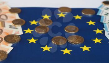 Euro banknotes and coins (EUR), currency of European Union over flag of Europe