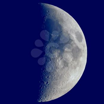 First quarter moon seen with an astronomical telescope, dark blue sky in square format